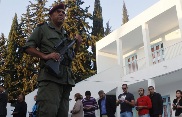 A Tunisian soldier stand guard as people stand in line at a polling station as they wait to cast their vote in the Ariyana district south of Tunis