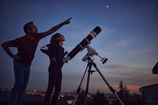 Silhouettes of father, daughter and astronomical telescope under starry skies.